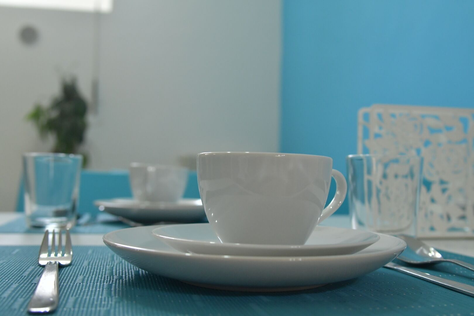 A dining table with a white cup and saucer, a glass, and cutlery.
