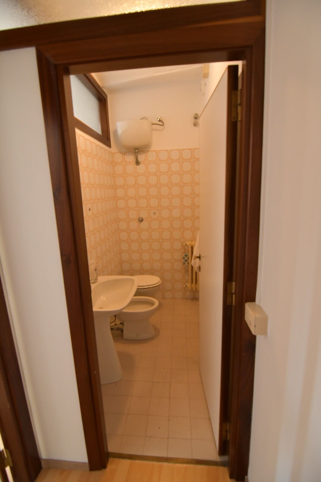 A narrow hallway leading to a bathroom with a toilet and sink.