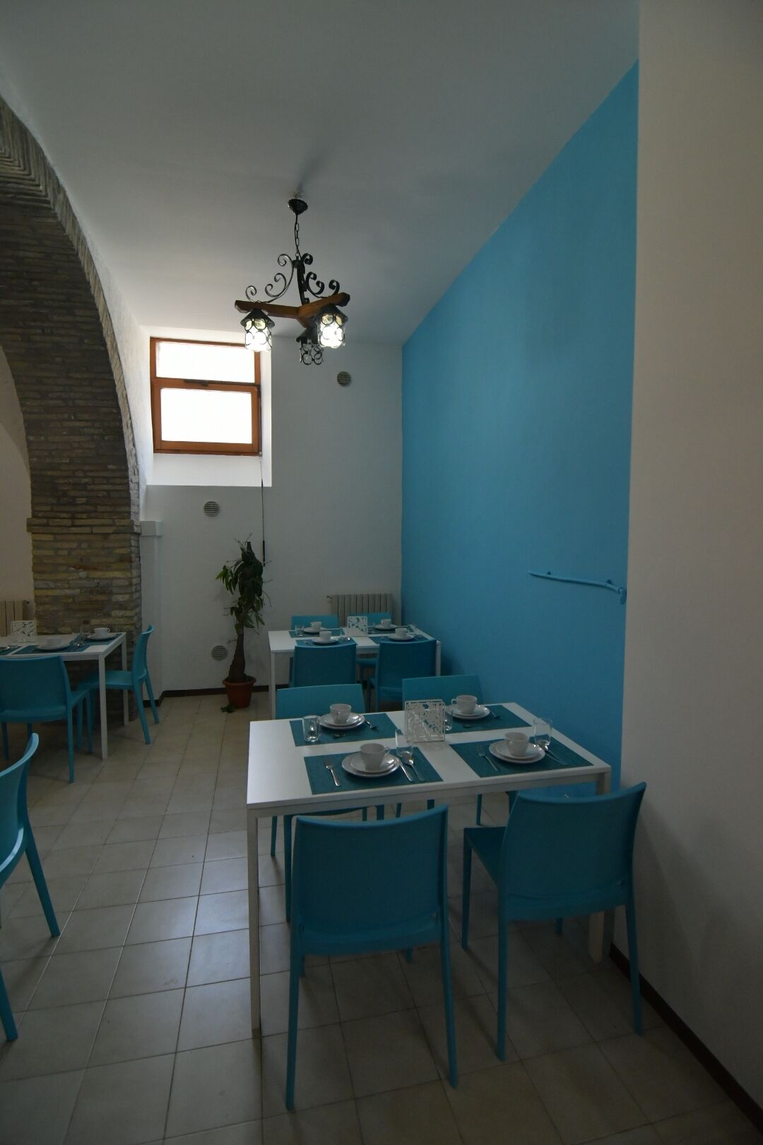 Zona pranzo con sedie e tavoli blu, una pianta in vaso e un lampadario.