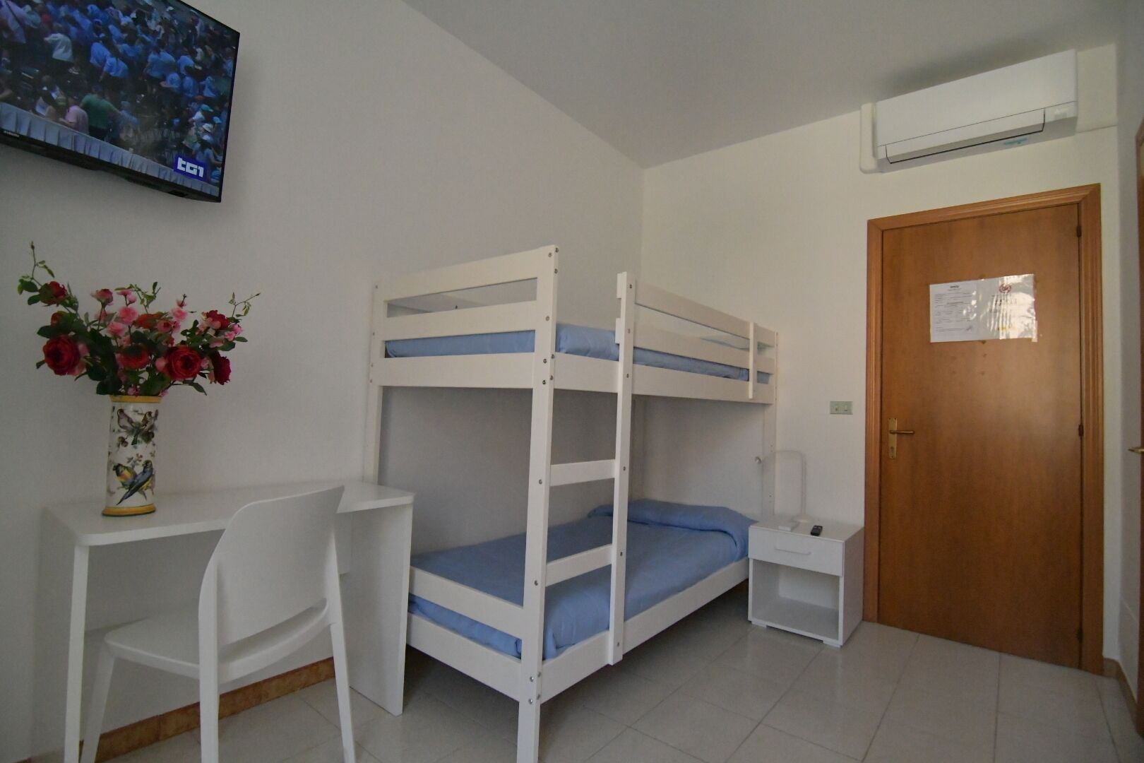 A bunk bed room with a desk, chair, and a TV on the wall.