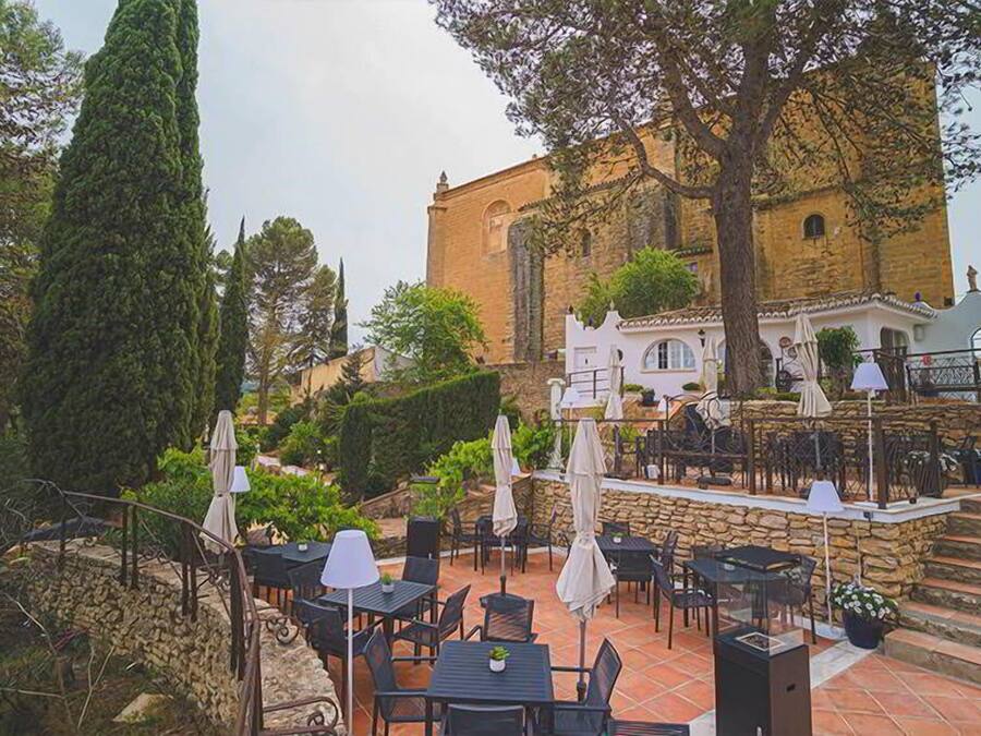 An outdoor patio with tables and chairs, surrounded by stone walls and greenery.