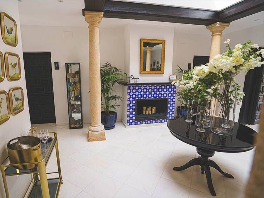 Un vestíbulo espacioso con una mesa redonda negra, una chimenea azulada con motivos decorativos y una obra de arte con marco dorado en la pared.