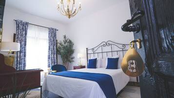 Une chambre d’hôtel avec un lit, un bureau, une chaise, une lampe, un lustre et une porte avec une serrure.