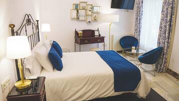 Habitación de hotel con cama, mesita de noche, lámpara, escritorio, silla y televisor en la pared.