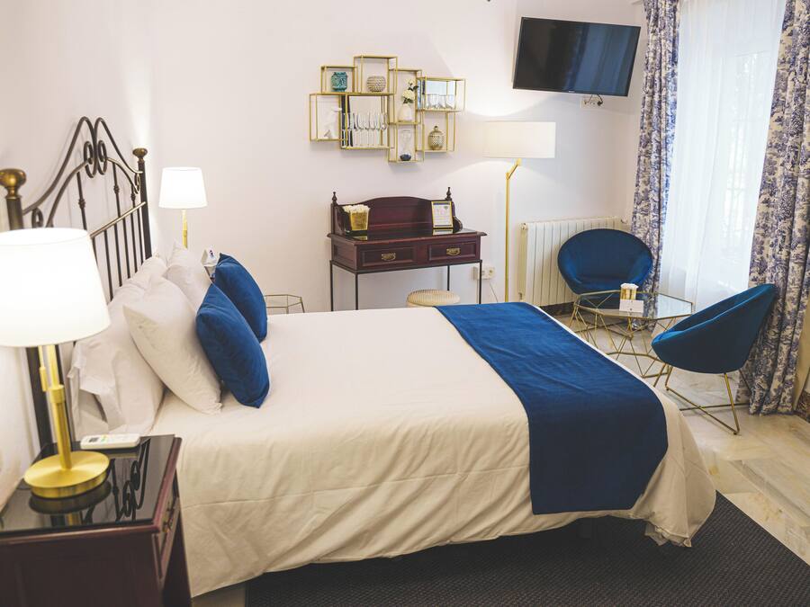 Habitación de hotel con cama, mesita de noche, lámpara, escritorio, silla y televisor en la pared.