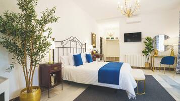 A bedroom with a bed, bedside table, lamp, potted plant, and a TV on the wall.