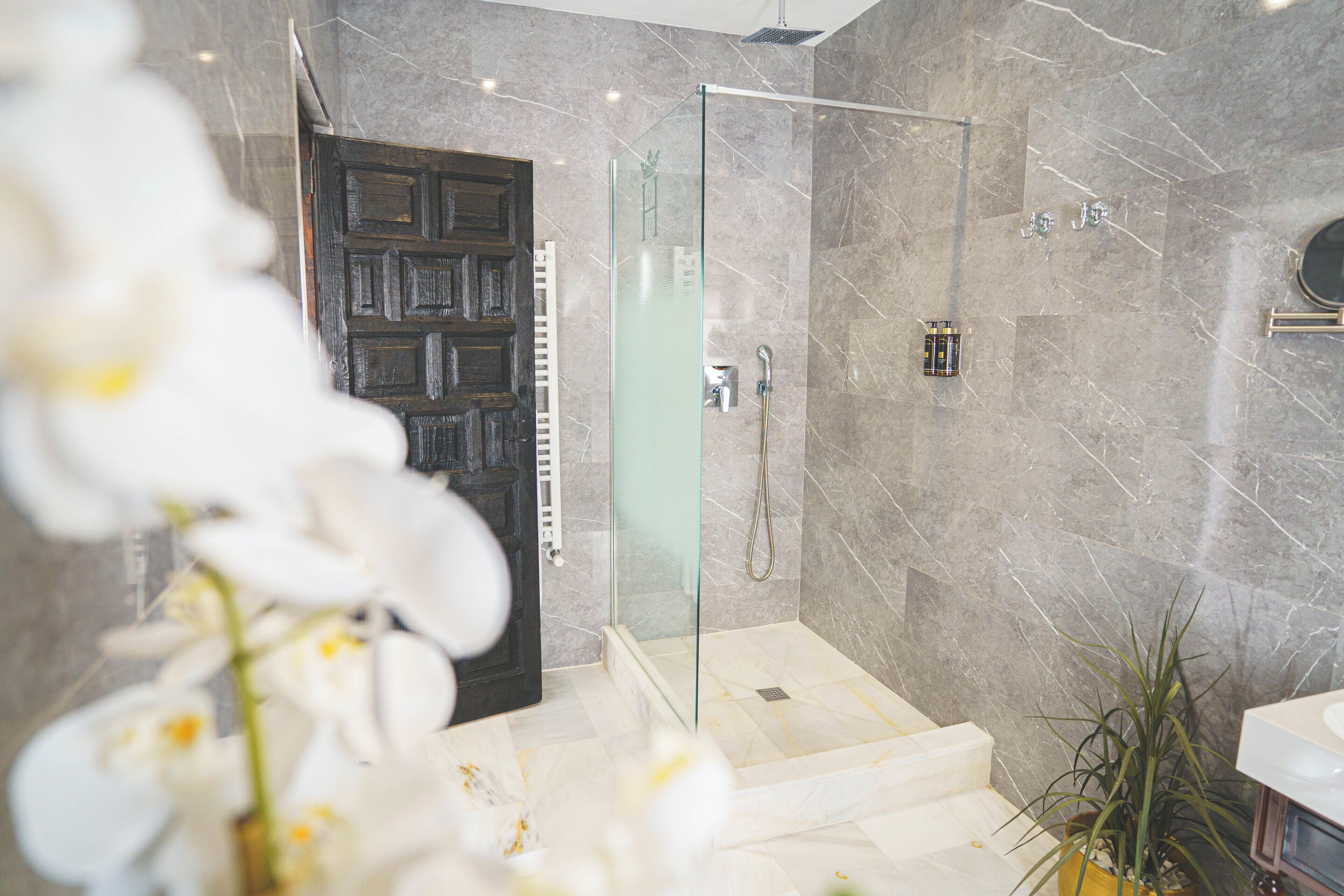 A modern bathroom with a glass-enclosed shower, marble walls, and a wooden door.