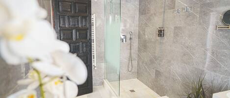 A modern bathroom with a glass-enclosed shower, marble walls, and a wooden door.