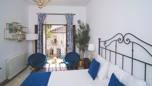 A hotel room with a bed, two chairs, a table, a chandelier, a radiator, and a view of the outside. - Hotel Boutique Palacio de la Duquesa (Ronda)