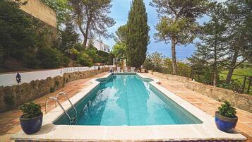 Una piscina rectangular con un suelo de baldosas, rodeada de muros de piedra y plantas en macetas.