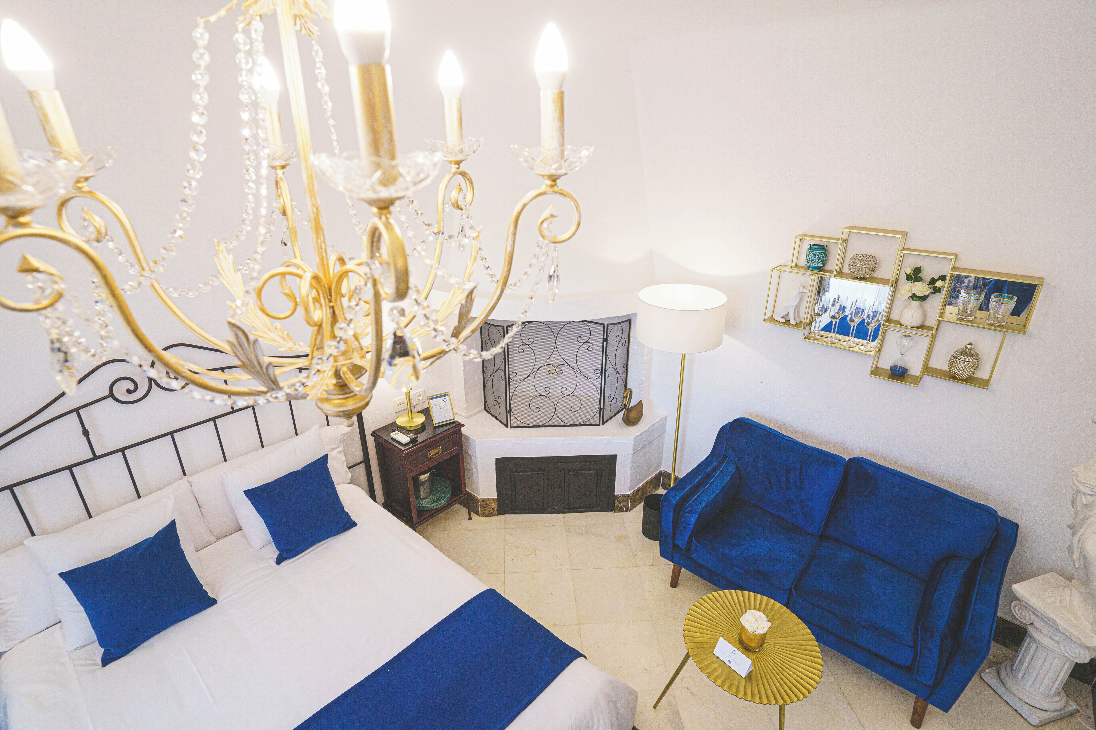 A hotel room with a bed, a blue sofa, a chandelier, and framed pictures on the wall.