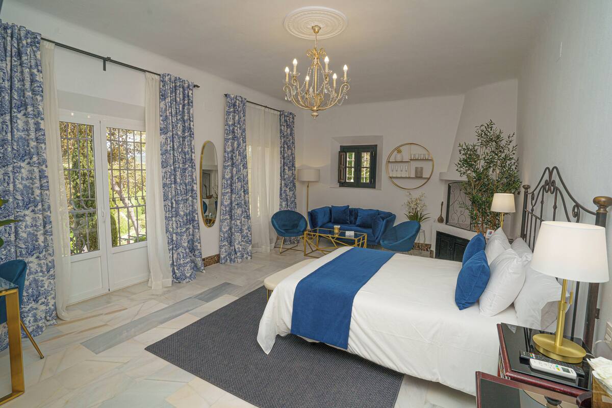 A bedroom with a large bed, a chandelier, a blue sofa, and a fireplace.