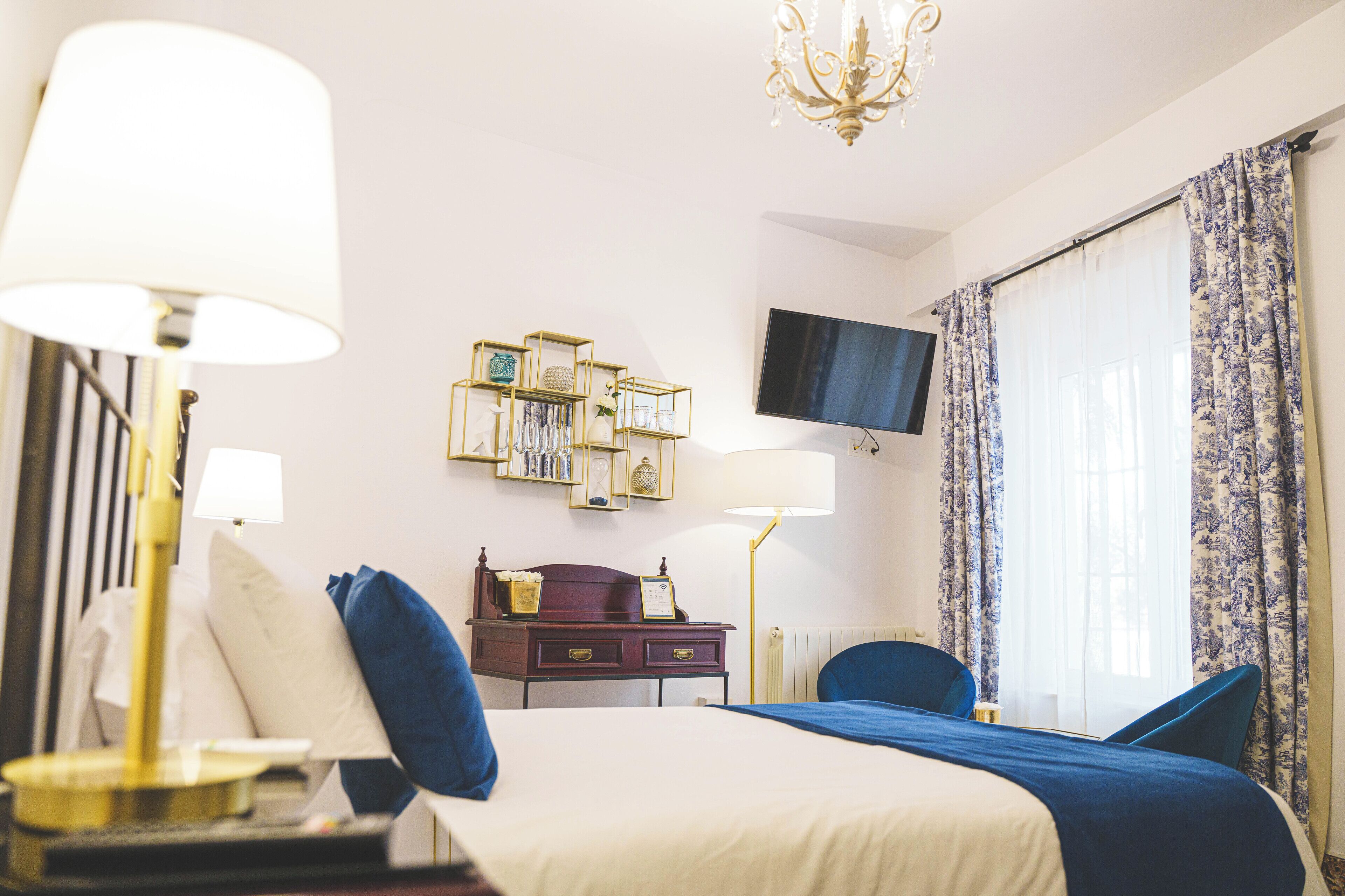 A hotel room with a bed, bedside lamps, a dresser, a television, and a window with curtains.