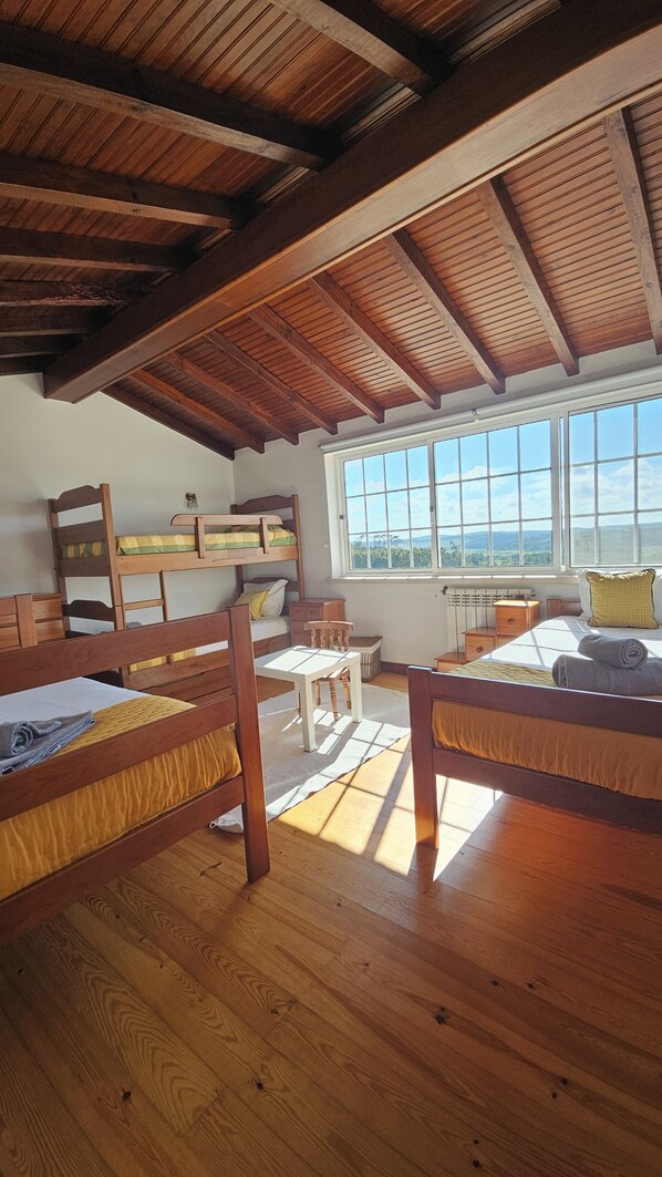 Una habitació amb llits superposats de fusta, una taula petita i una finestra que mostra el paisatge exterior.