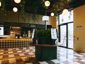 A modern interior with a checkered floor, a reception desk, a menu board, and hanging plants.