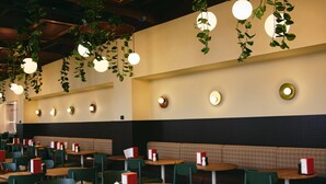 Un restaurante con suelo a cuadros, sillas verdes, mesas de madera y plantas colgantes.