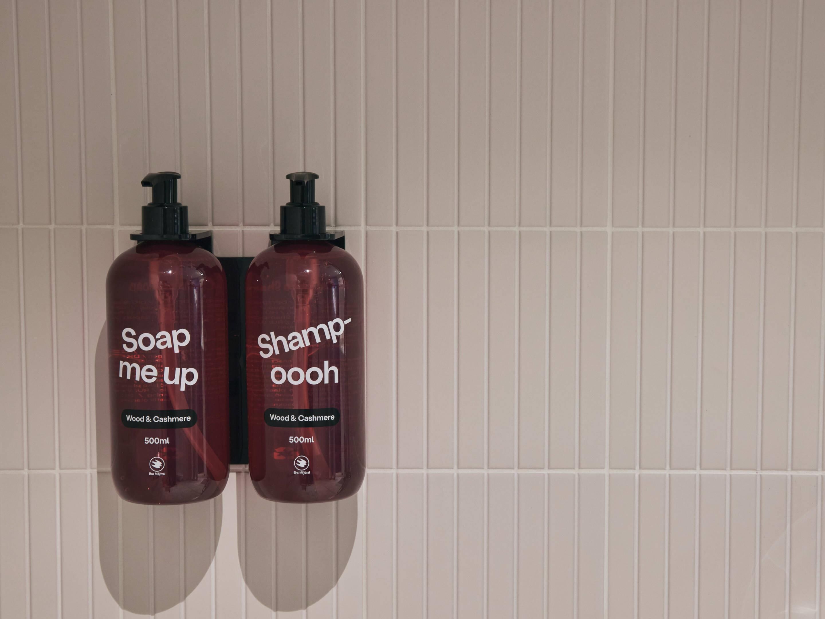 Duas garrafas de shampoo e sabonete em frente a uma parede de azulejos.