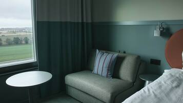 A hotel room with a green sofa, a small round table, a bed, and a view of the countryside through a window.