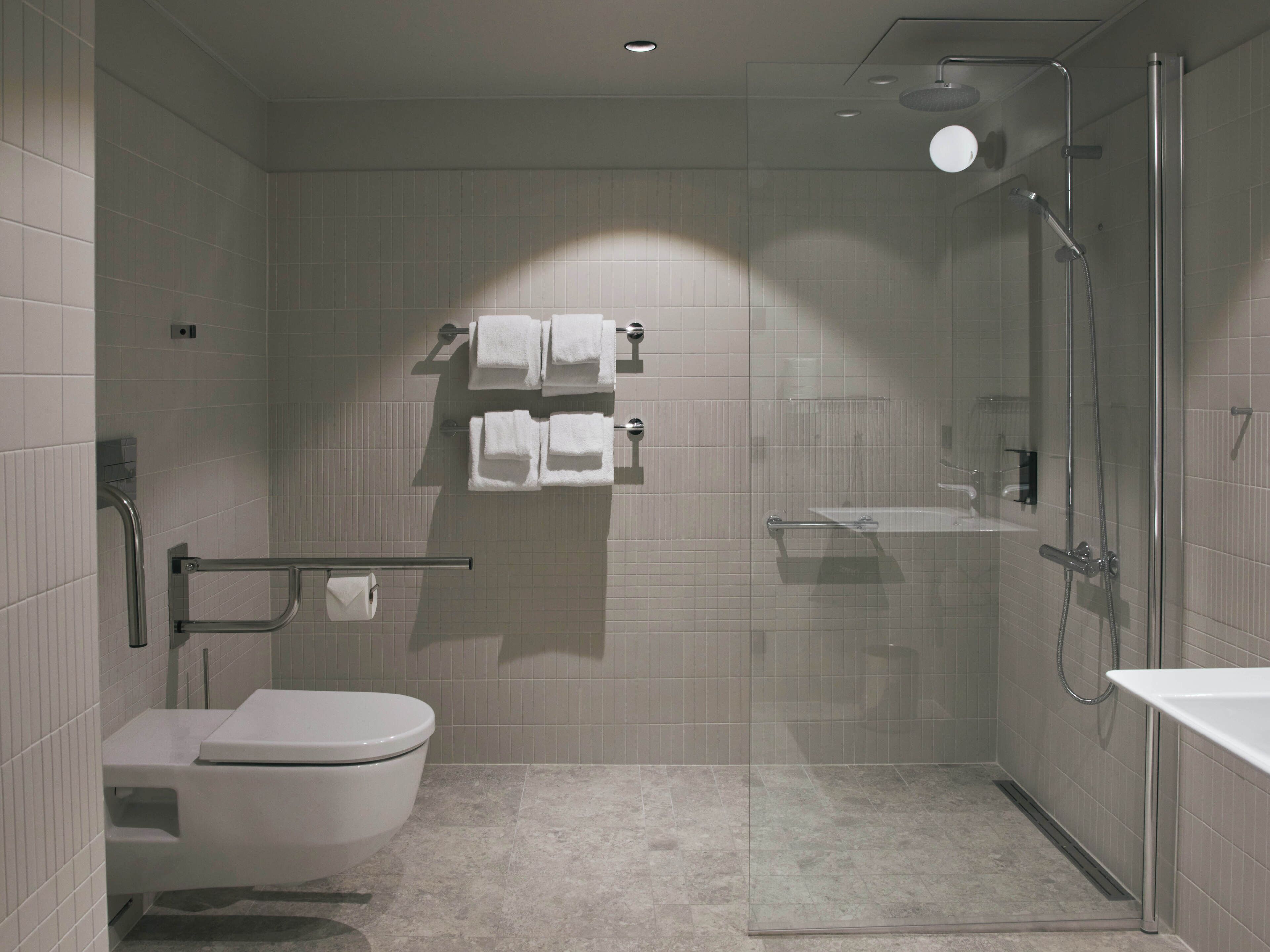 Un baño moderno con inodoro, cabina de ducha de vidrio y toallero con varias toallas.