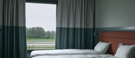 Habitación de hotel con cama, cortinas, una ventana que da a un paisaje verde y un aplique de techo.