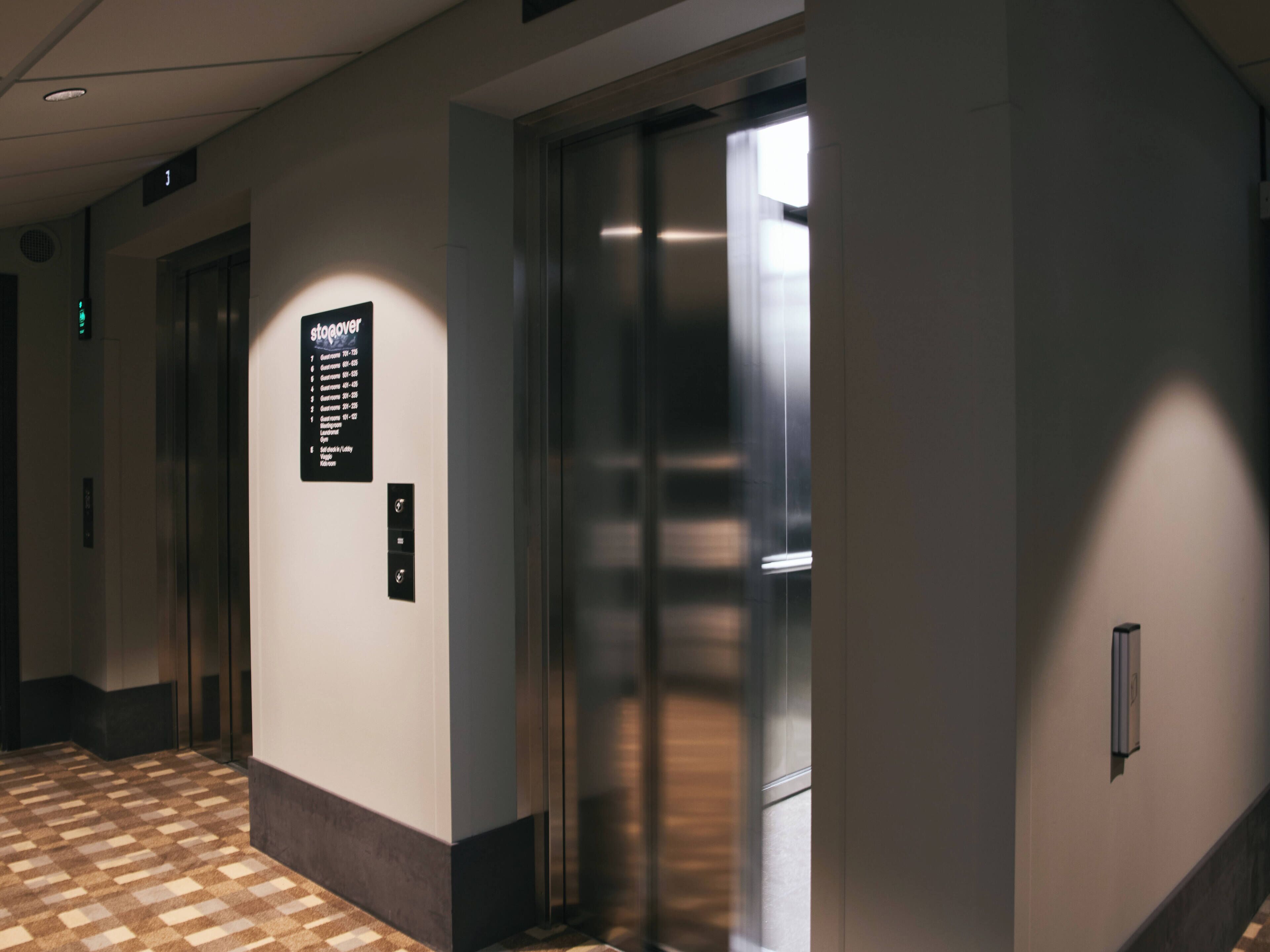 A hallway with an elevator and a sign indicating the number of customers in each direction.