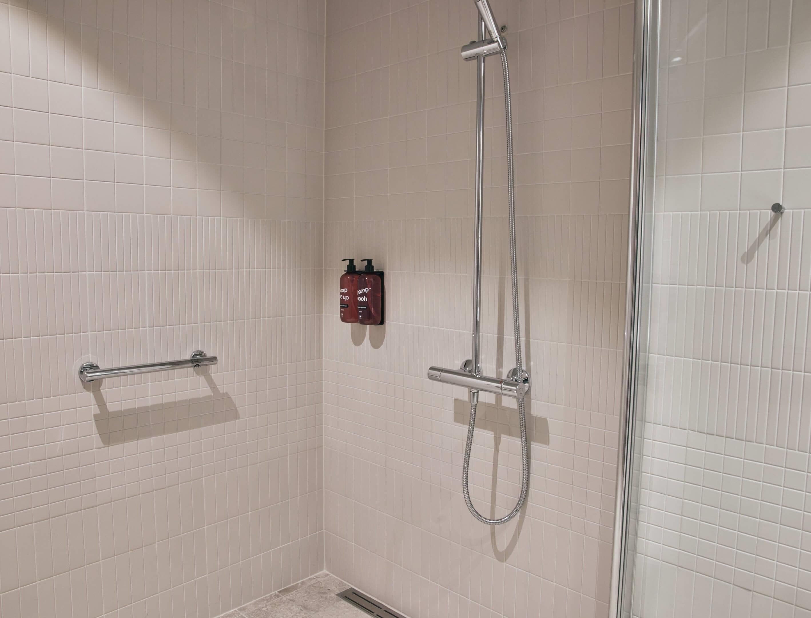 A shower area with a glass door, a handheld showerhead, and two bottles of shampoo on the wall.