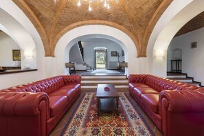 Un salón espacioso con sofás de cuero rojo, alfombra estampada y techo de ladrillo.