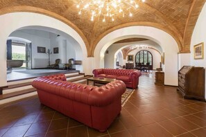 Un vestíbulo espacioso con sofás de cuero rojo, un candelabro y techos abovedados.