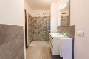 Un baño con ducha, lavamanos, espejo y toalla.