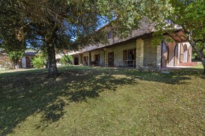 A stone building with a covered porch, a lawn, and trees.