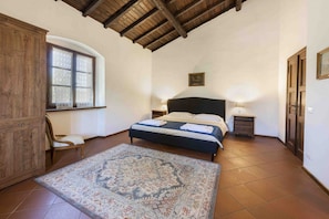A bedroom with a bed, a wooden wardrobe, a chair, a window, and a rug.