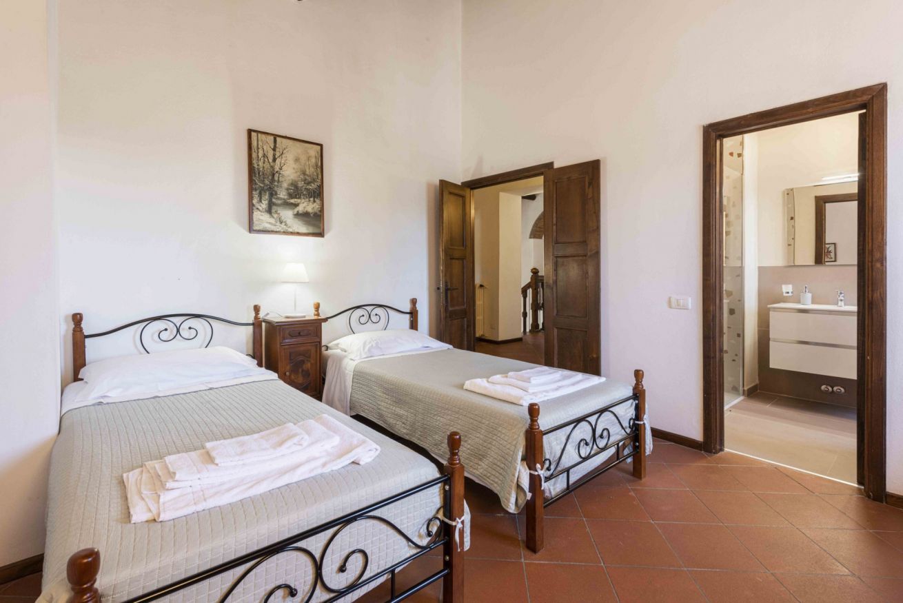 Una camera da letto con due letti, un quadro, uno specchio e un bagno visibile attraverso una porta aperta.