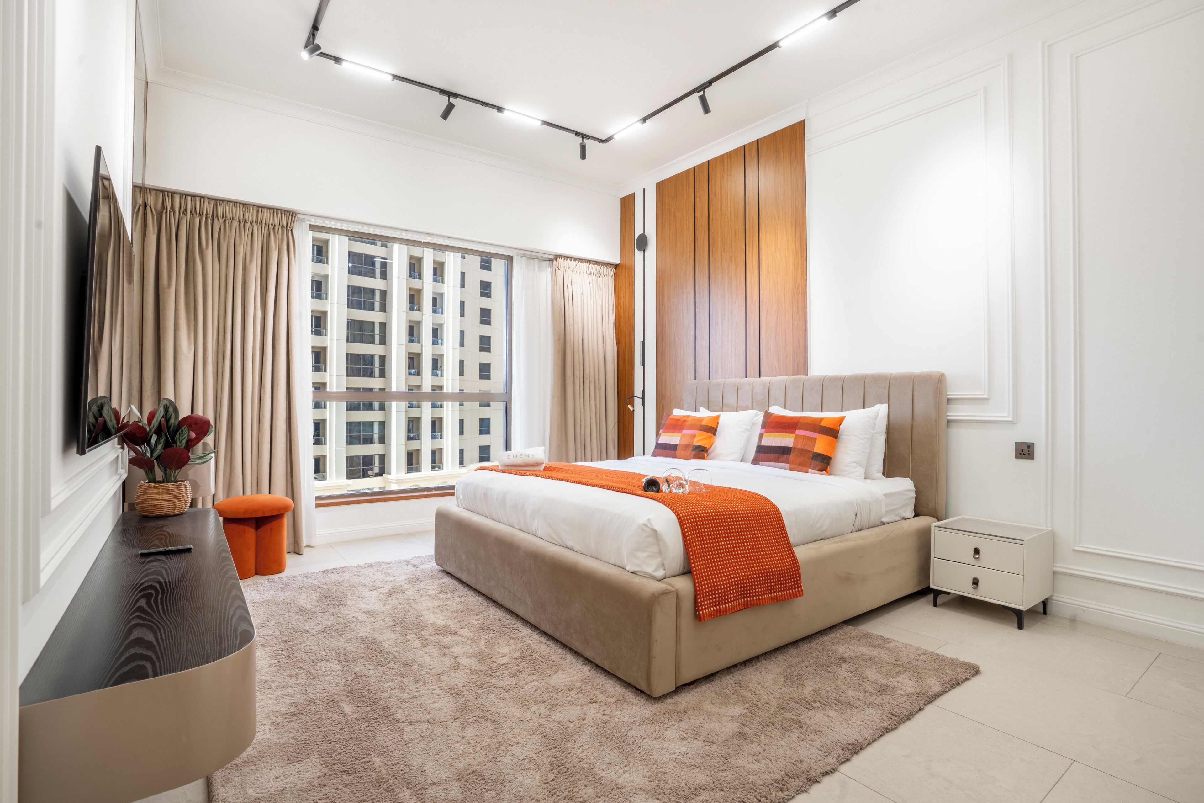 A modern bedroom with a large bed, a nightstand, a dresser, and a window with curtains.
