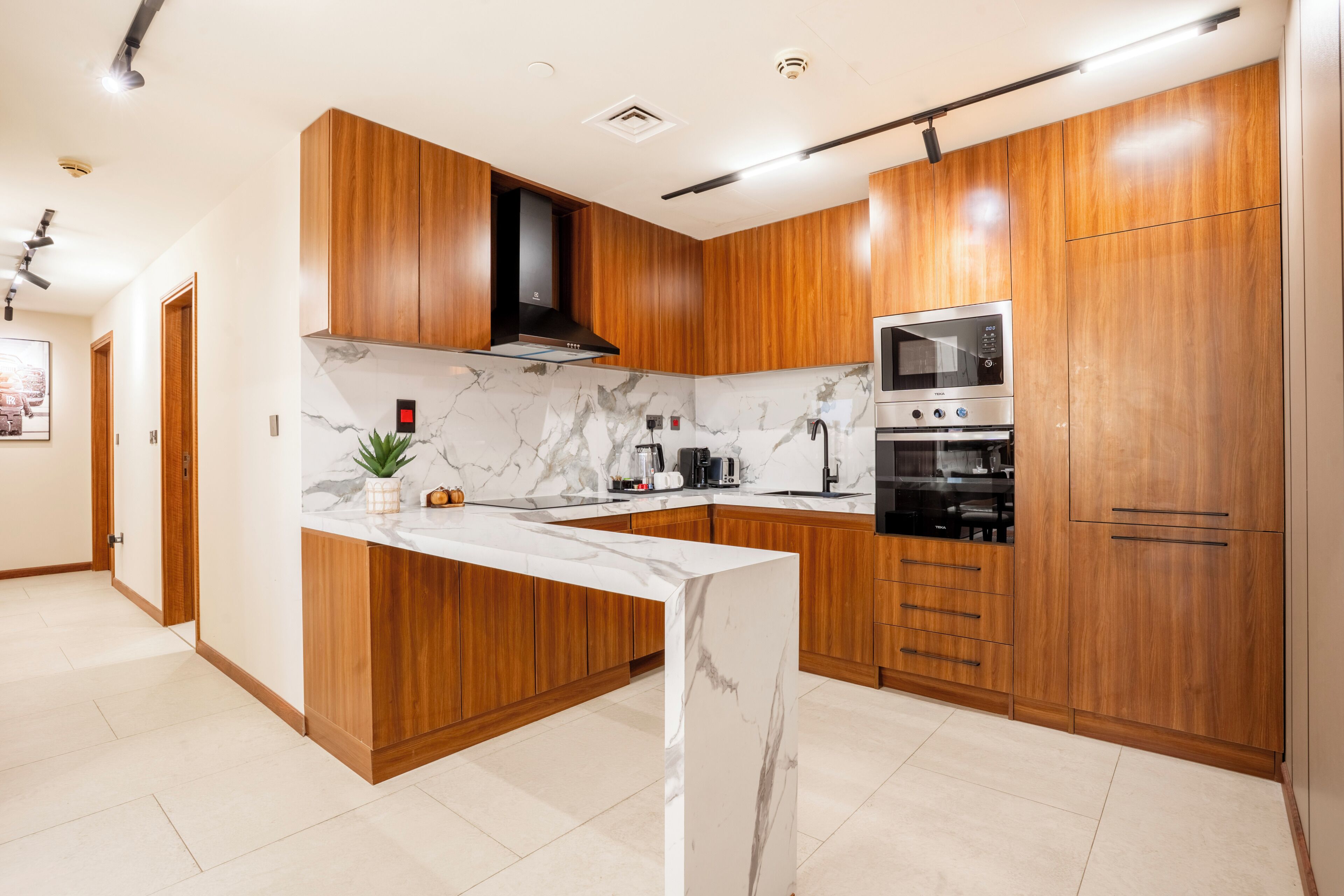 A modern kitchen with wooden cabinets, a marble countertop, a built-in microwave, and a stove.