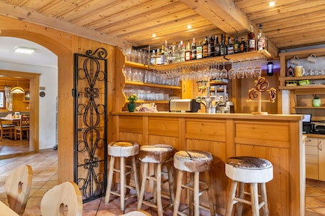 A wooden bar area with stools, a bar counter, and shelves of bottles and glasses.