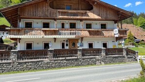 Un edificio de madera de varios pisos con balcones, un muro de piedra en primer plano y un cielo despejado.