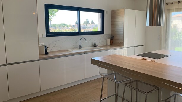 Una cocina moderna con armarios blancos, un ventanal amplio y una isla de madera con taburetes de bar.
