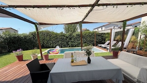 Un espacio al aire libre techado con piscina, terraza de madera y disposición de asientos.