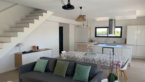 Un apartamento moderno con una escalera, una sala de estar con sofá y mesa de centro, una cocina con comedor, y un ventanal que ofrece vistas.
