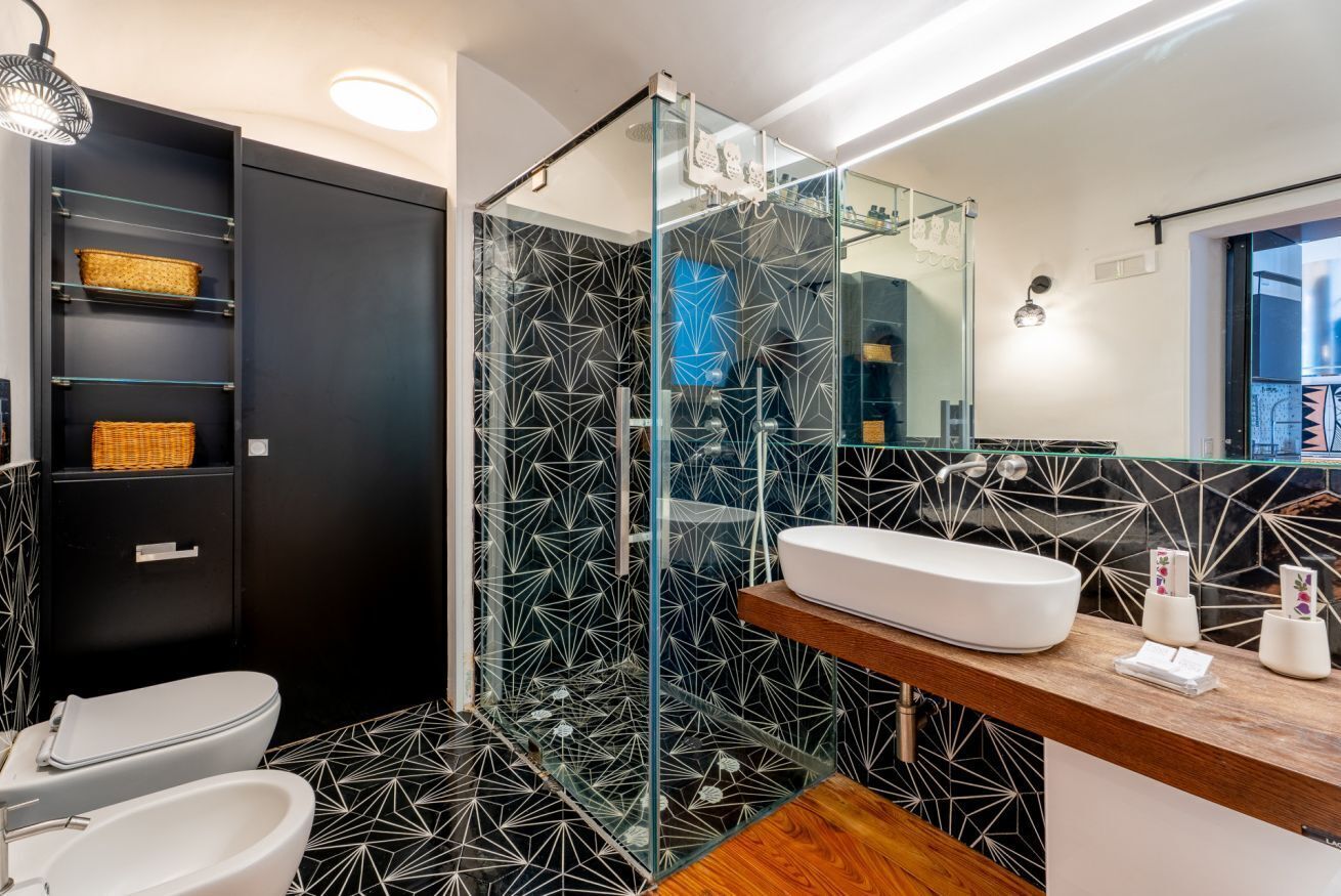 Een moderne badkamer met een glazen douchecabine, een wit wastafelmeubel en een zwart-wit betegelde spatwand.
