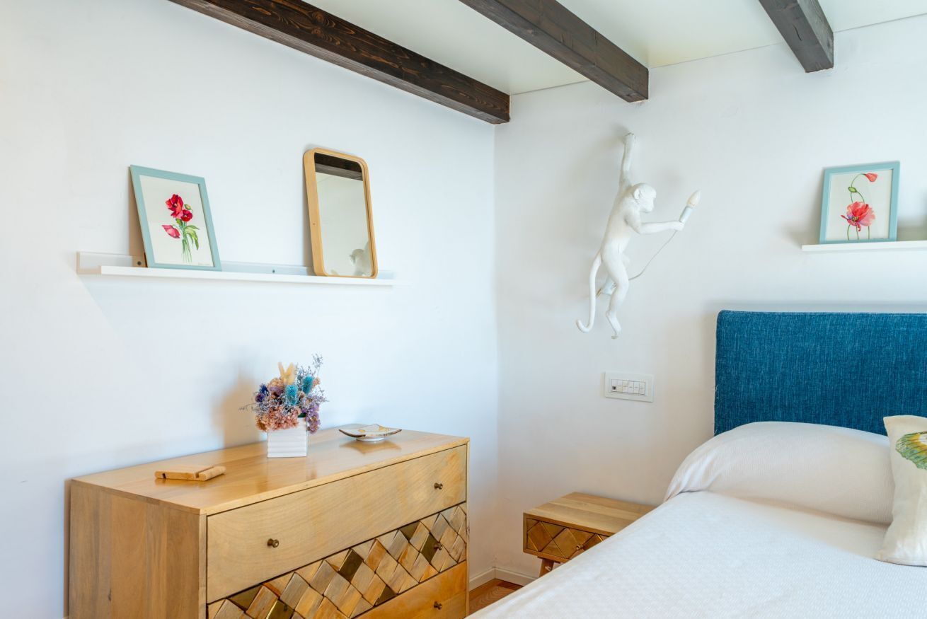 Une chambre avec une commode en bois, un lit doté d’une tête de lit bleue, une sculpture fixée au mur et des œuvres d’art encadrées accrochées au mur.