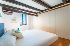 Une chambre à coucher avec un lit, une fenêtre, des poutres en bois et un tableau accroché au mur.