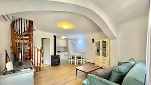 Un salon avec un canapé vert, un plancher en bois, un escalier et un coin cuisine doté de meubles blancs.