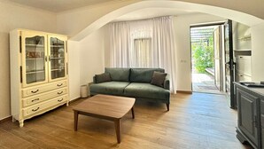 Un salon avec un canapé vert, une table basse en bois, un meuble de couleur crème doté de portes en verre et une porte en arc donnant sur un balcon.