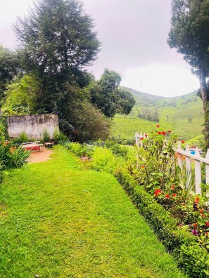 A lush garden with a variety of plants and flowers, a white fence, and a view of a green hillside in the background. - Amber by The Tamarillo (Ooty)