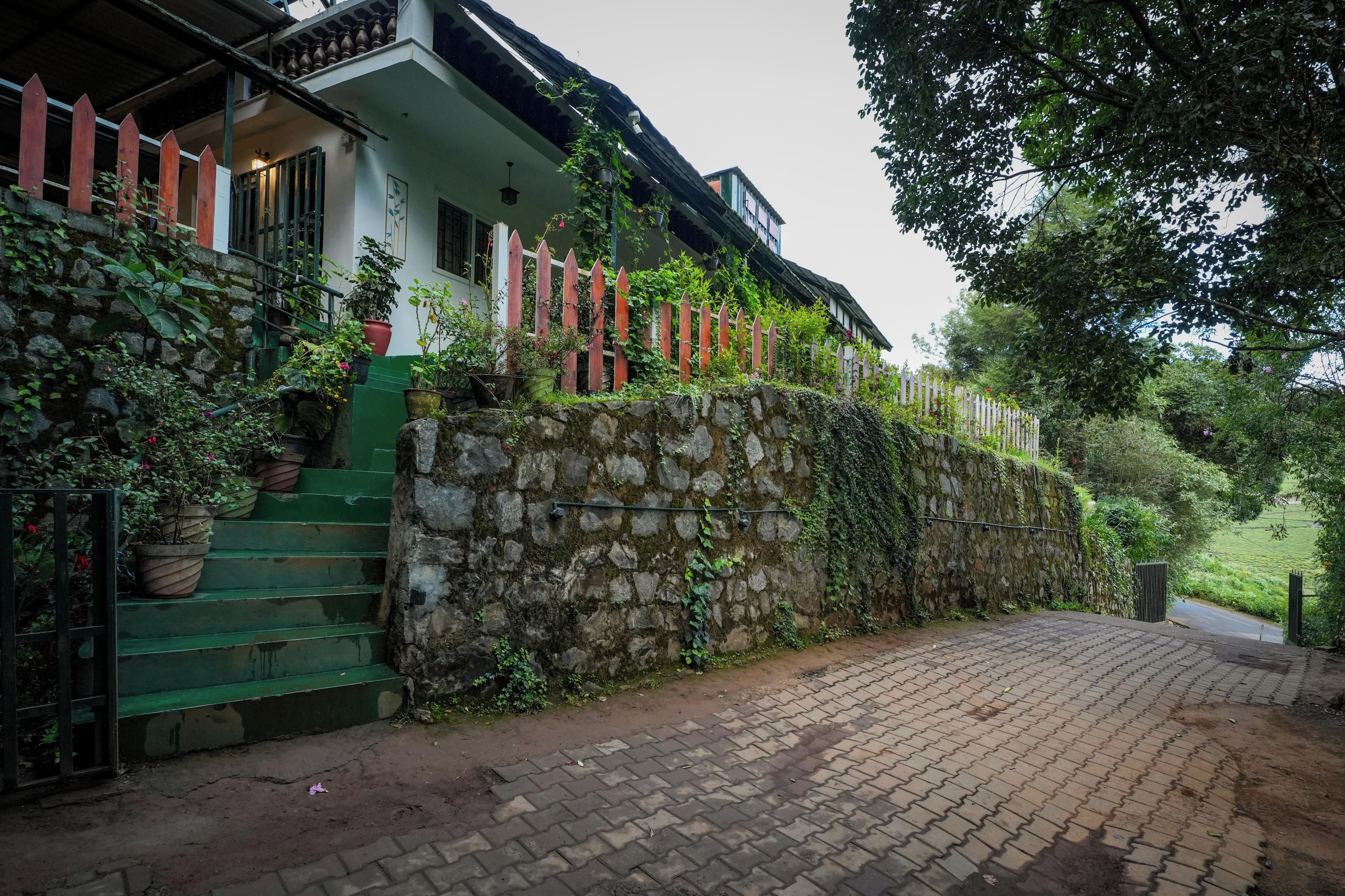 Una casa con pared de piedra, cerca de madera y camino de entrada pavimentado.