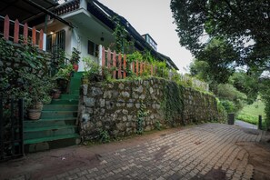 A house with a stone wall, a wooden fence, and a paved driveway. - Amber by The Tamarillo (Ooty)