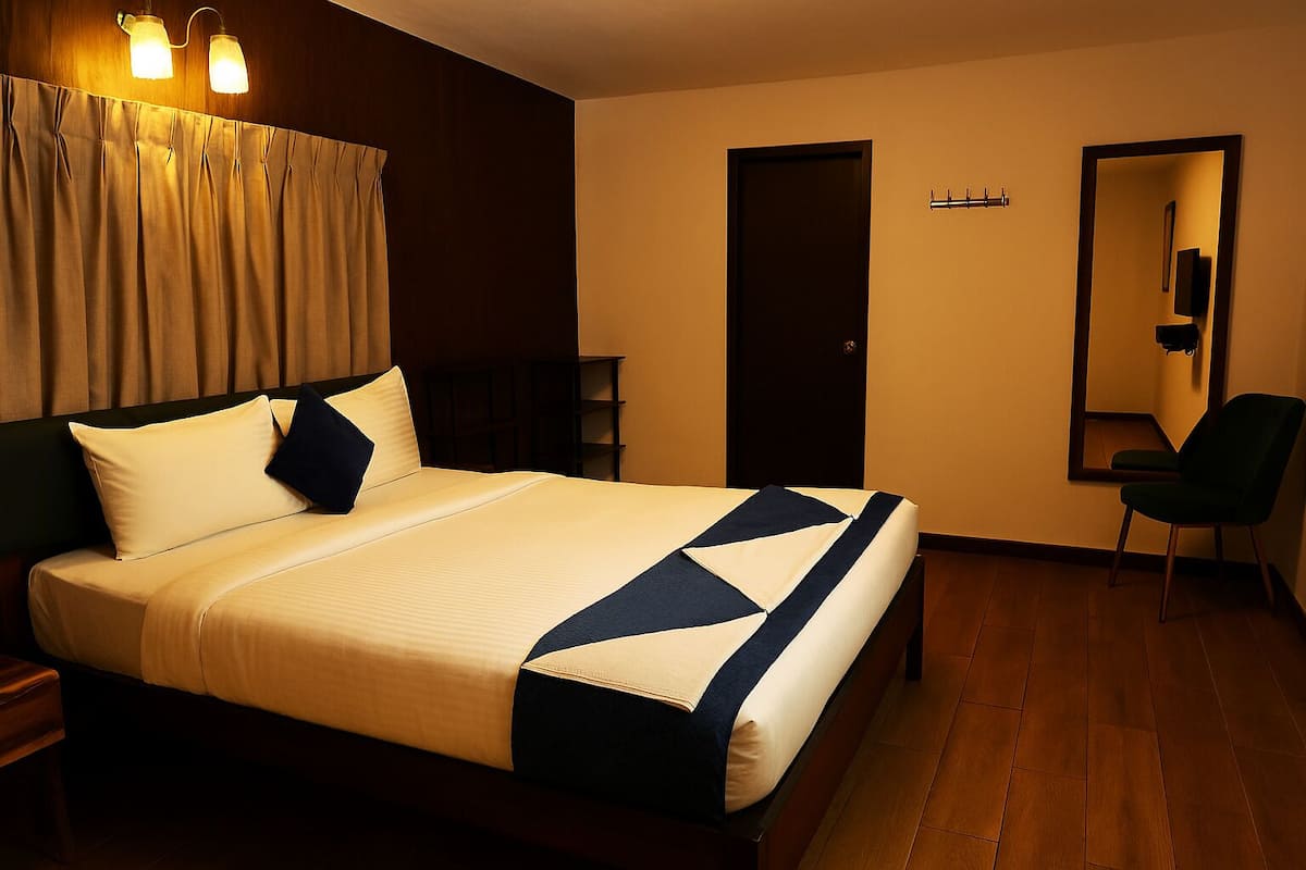 A neatly made bed with a striped bedspread, a dark green chair, a wooden floor, and a door with a mirror.