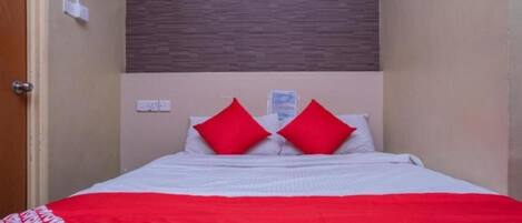 A bed with white bedding and red accents, a wooden headboard, and a brown textured wall.