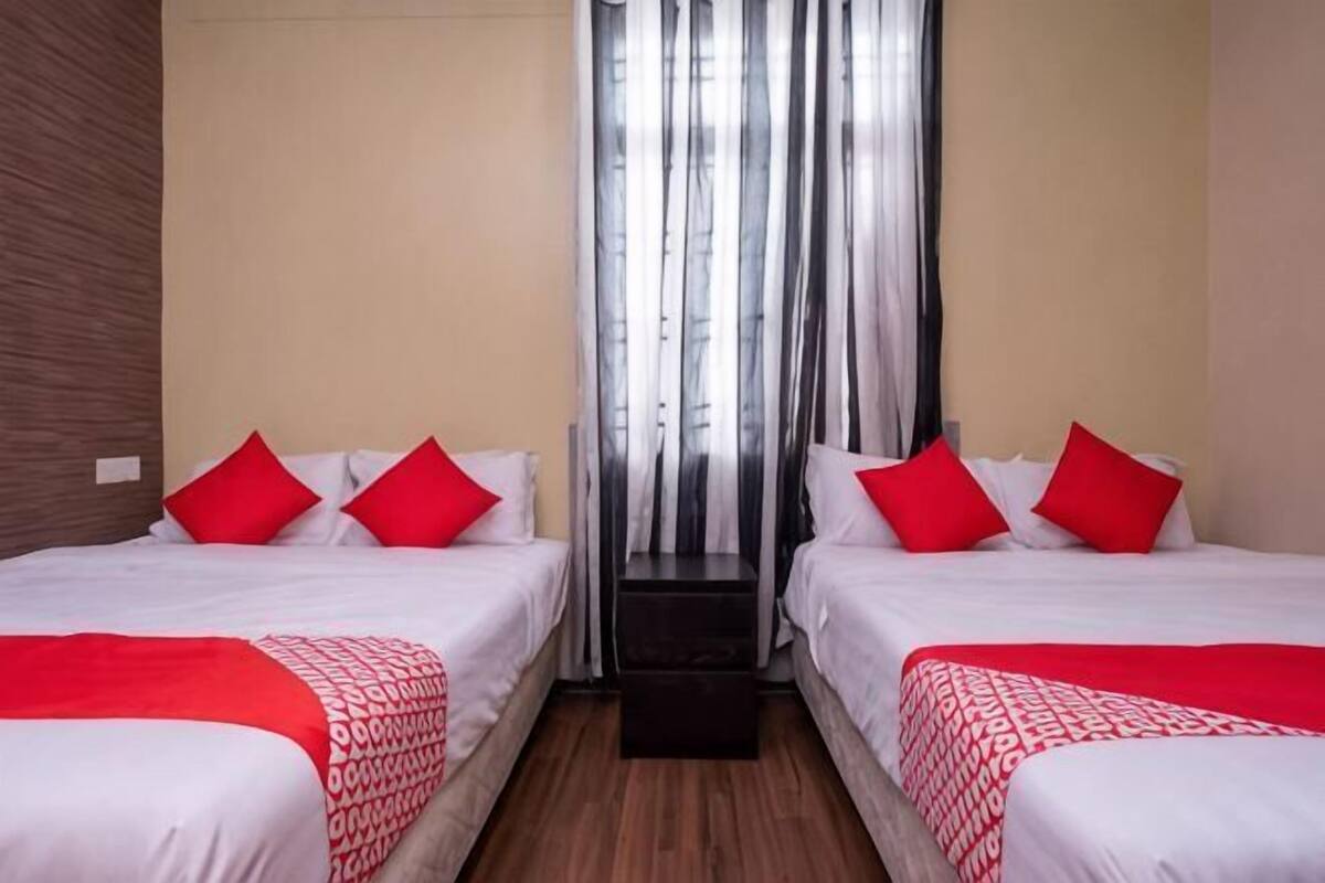 A hotel room with two beds, red and white bedding, a wooden floor, and a window with vertical blinds.